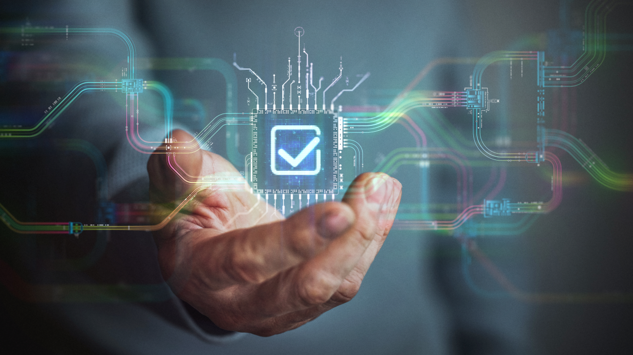 Male hand holding futuristic check mark icon in the center and circuit board with vibrant data transfers representing evolving assistance technology of the future