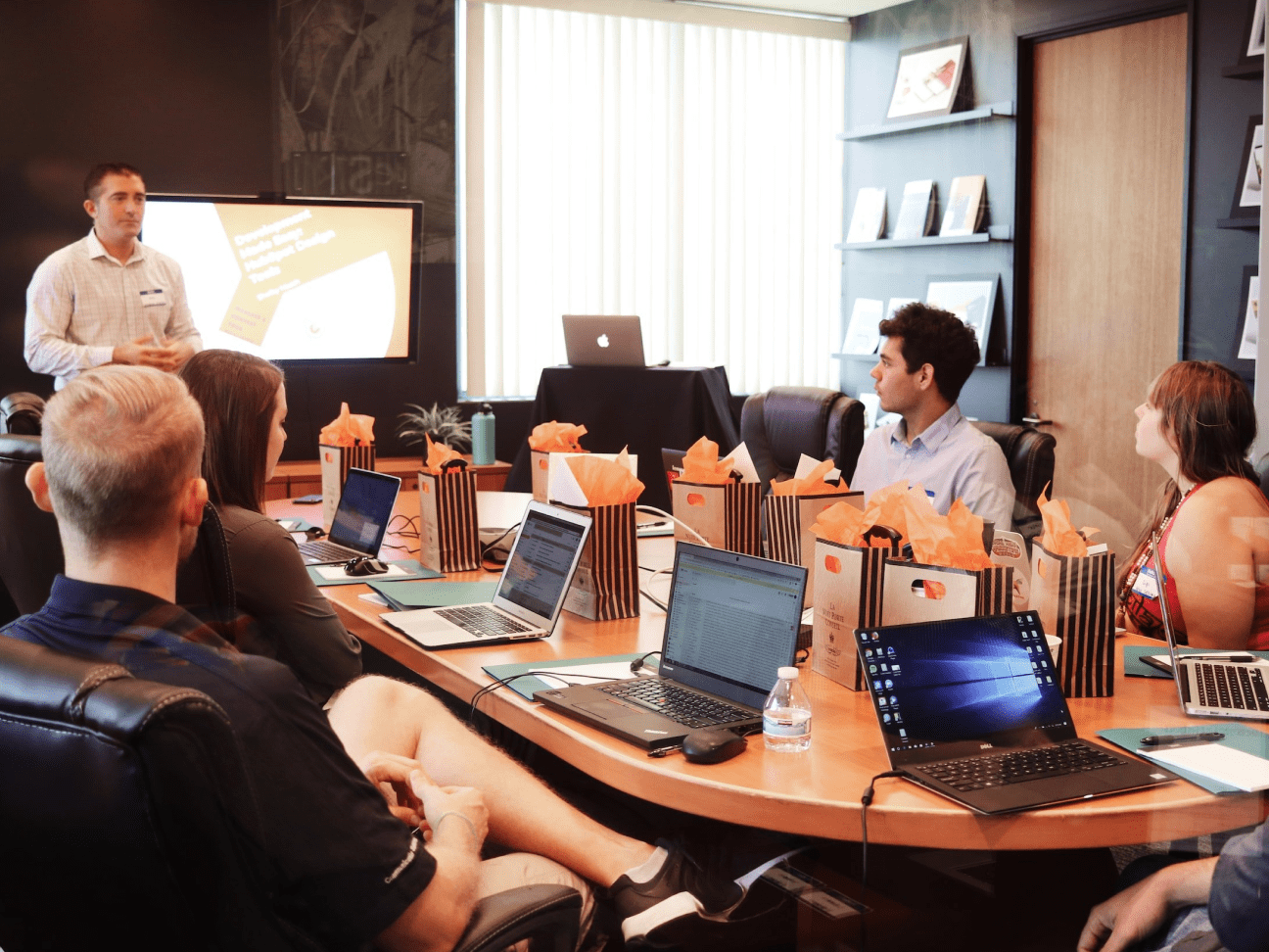 People seated around a meeting table having a discussion with laptops open